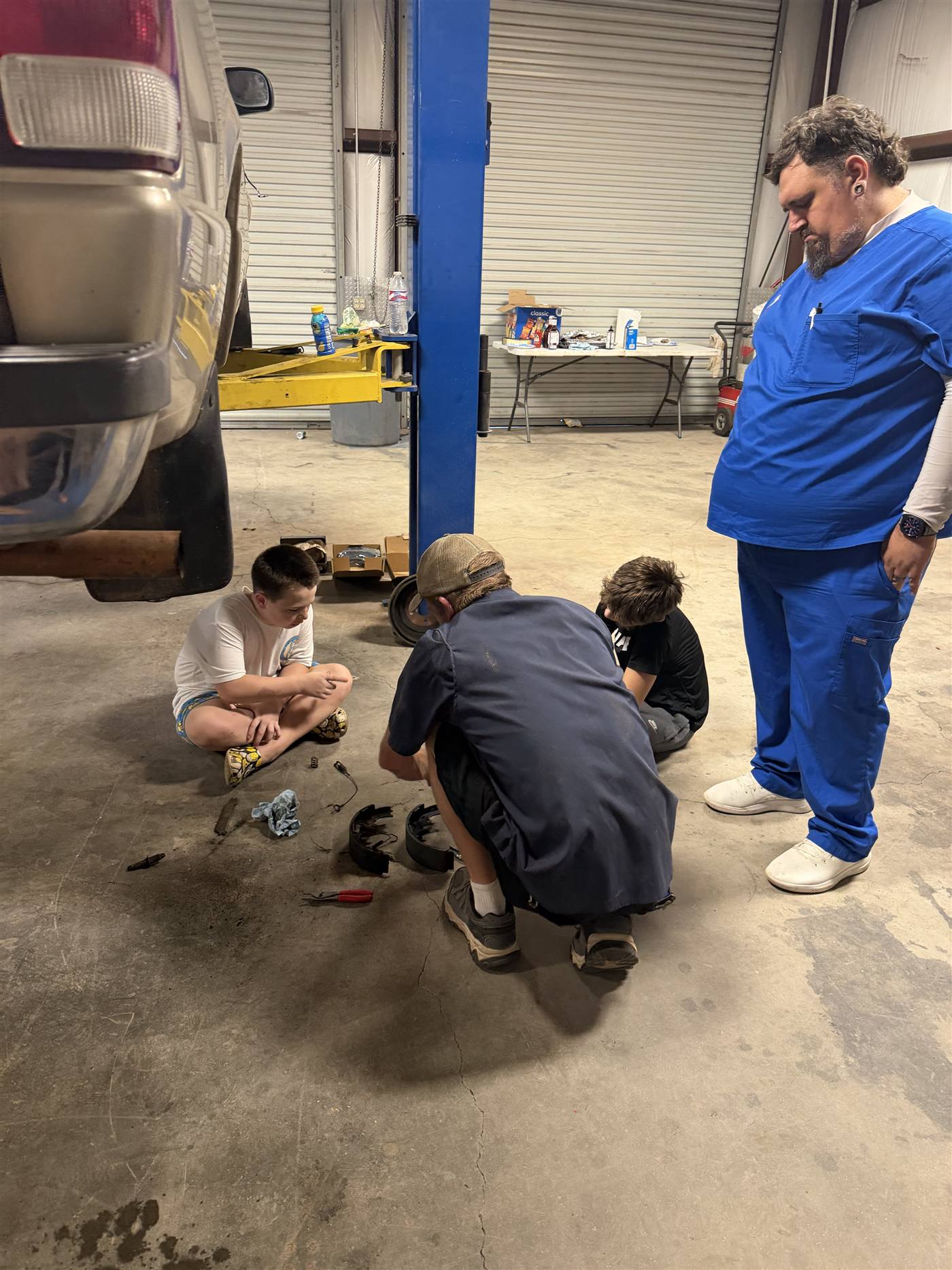 Youth and mentors kneeling on the shop floor examining brake shoes and springs laid out in front of them