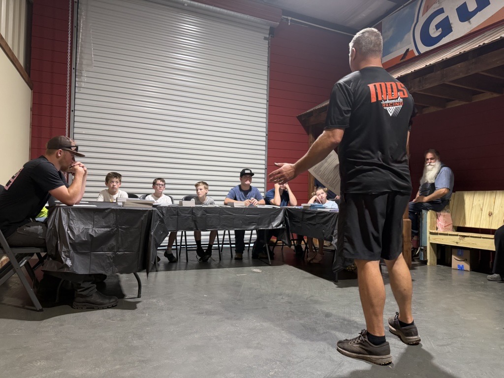 Jerry speaking to a row of youth seated at tables in the shop, gesturing as he talks